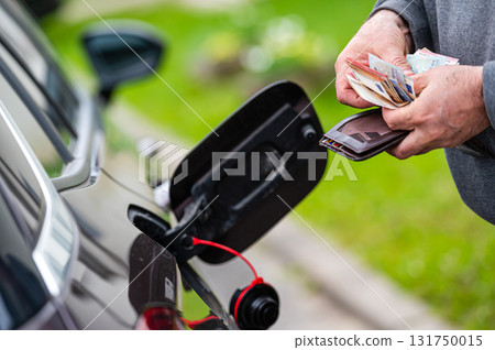 a man counts money standing at an open fuel tank, the concept of rising fuel prices, closeup 131750015