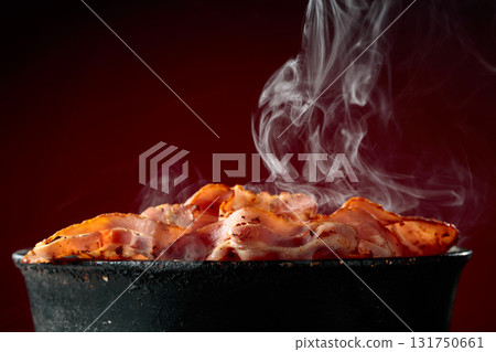 Fried steaming bacon slices in an old black pan. Fried steaming bacon slices in an old black pan. 131750661