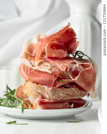 Ciabatta with prosciutto and rosemary on a white wooden table. Ciabatta with prosciutto and rosemary on a white wooden table. 131750664