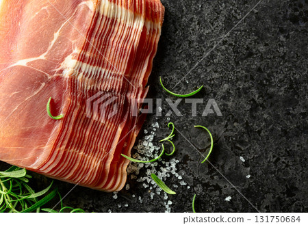 Sliced prosciutto and rosemary on a stone table. 131750684