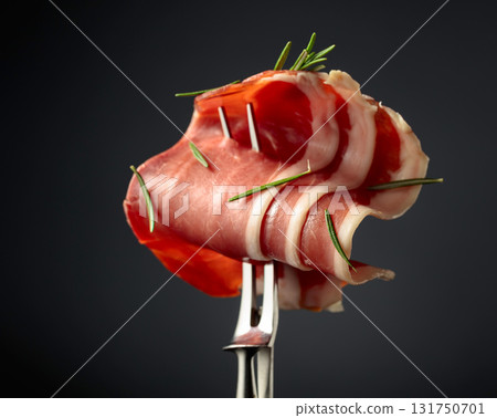 Sliced prosciutto with rosemary on a fork. 131750701