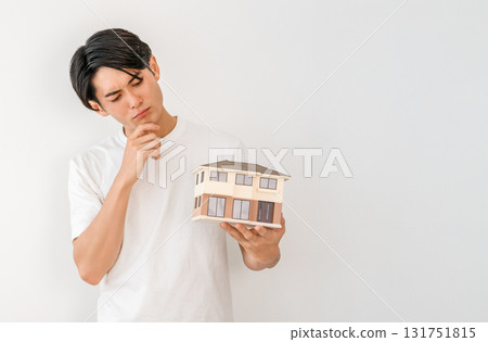 Young Asian man holding a house model (my home, detached house, house building, failure, regret, trouble) Young Asian man holding a house model (my home, detached house, house building, failure, regret, trouble) 131751815