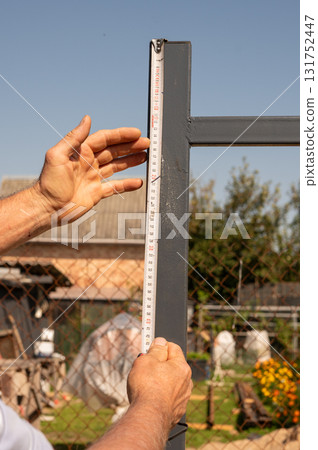 Adult male measuring metal fence with tape measure in garden setting Adult male measuring metal fence with tape measure in garden setting 131752447