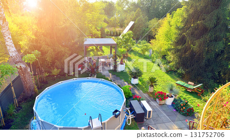Garden of a suburban house in summer in which you can see a removable swimming pool, pergola in a place with a lot of vegetation. 131752706