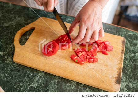 Caucasian female cutting tomato on wooden board in kitchen setting 131752833