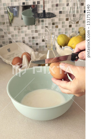 Anonymous person prepares dough in bowl and cracks an egg with knife. Healthy eating with organic, gluten-free ingredients. Home cooking. 131753140