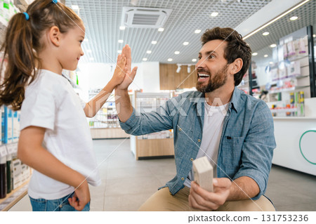 Smiling Caucasian father with little girl standing near counter in pharmacy Smiling Caucasian father with little girl standing near counter in pharmacy 131753236