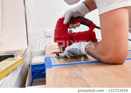 repairman with electric jigsaw doing sawing place for installing hob in a worktop in the kitchen repairman with electric jigsaw doing sawing place for installing hob in a worktop in the kitchen 131753836