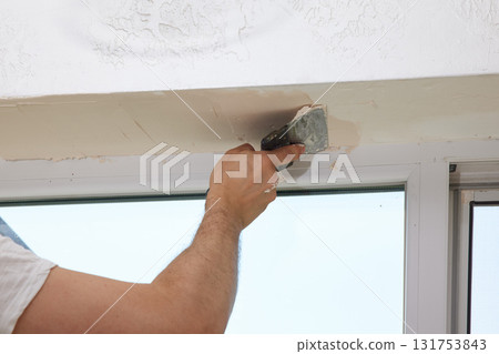 Caucasian plasterer man with a spatula applying finishing putty on a window opening 131753843