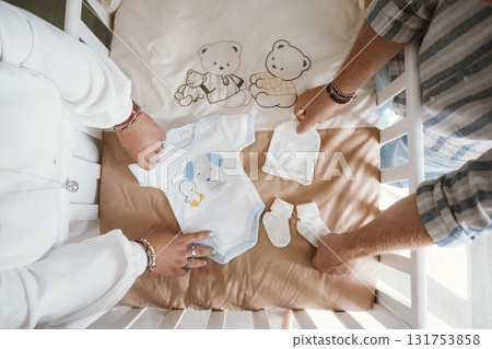 Parents Preparing Baby Crib with Clothes and Accessories 131753858