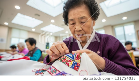 Elderly Korean woman in purple cardigan doing detailed embroidery needlework with colorful floral patterns in bright community center crafts room 131754035