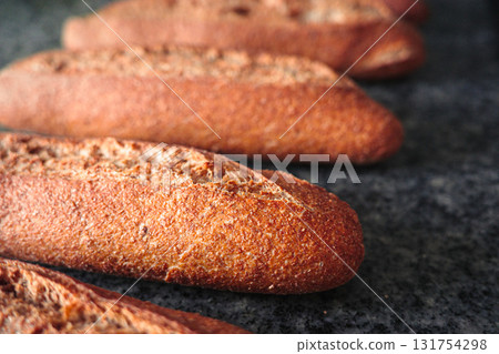 Close-up of freshly baked whole wheat bread rolls on a dark kitchen counter, rustic homemade food background 131754298