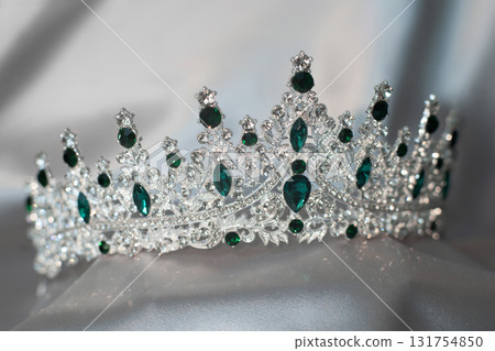 Crown with emerald green gemstones on grey background. Jewelry 131754850