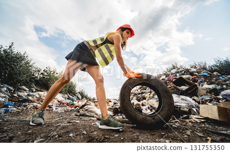 Woman volunteer helps clean the field of plastic garbage and old tires.  131755350