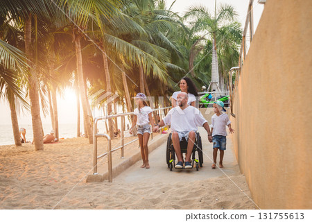 Disabled man in a wheelchair moves on a ramp to the beach with his family. 131755613