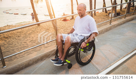 Disabled man in a wheelchair moves on a ramp to the beach. Disabled man in a wheelchair moves on a ramp to the beach. 131755614