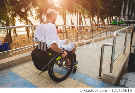 Disabled man in a wheelchair moves on a ramp to the beach. Disabled man in a wheelchair moves on a ramp to the beach. 131755619