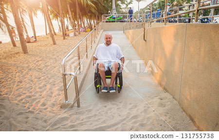 Disabled man in a wheelchair moves on a ramp to the beach. Disabled man in a wheelchair moves on a ramp to the beach. 131755738