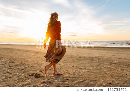 Stylish woman walks at sunset along beach of sea on at sunset. Travel, relax and lifestyle concept. Stylish woman walks at sunset along beach of sea on at sunset. Travel, relax and lifestyle concept. 131755751