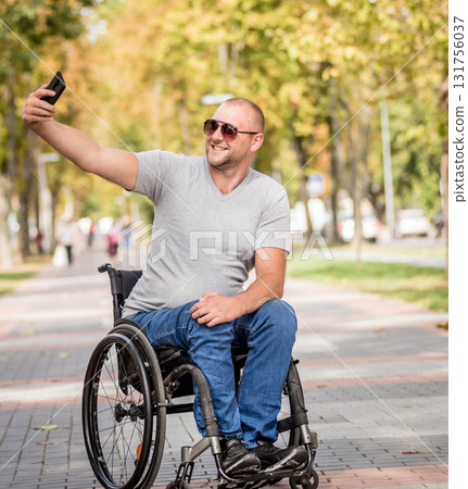 Handicapped man in wheelchair at the park alley use a smartphone Handicapped man in wheelchair at the park alley use a smartphone 131756037