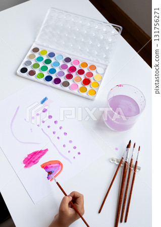 Child painting with watercolors on paper. Art supplies and creativity at play Child painting with watercolors on paper. Art supplies and creativity at play 131756271