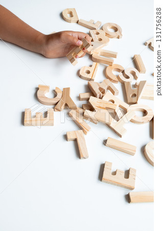 Child hand arranging wooden alphabet letters on white surface 131756288
