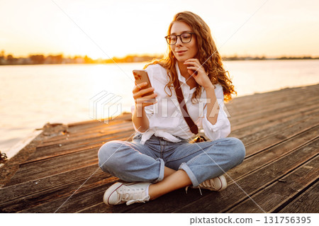 Young woman uses phone walk on embankment. Concept of vacation, technology, weekend. Young woman uses phone walk on embankment. Concept of vacation, technology, weekend. 131756395