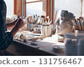 A sculptor's hands form clay at a desk in a brightly lit art studio 131756467