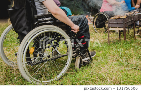 Disabled man resting in a campsite with friends. Wheelchair in the forest Disabled man resting in a campsite with friends. Wheelchair in the forest 131756506