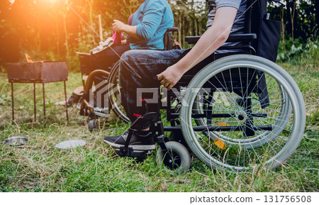 Disabled man resting in a campsite with friends. Wheelchair in the forest Disabled man resting in a campsite with friends. Wheelchair in the forest 131756508