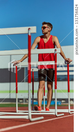 Male athlete standing between hurdles on track wearing red uniform Male athlete standing between hurdles on track wearing red uniform 131756824