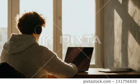 Person Wearing Headphones Working on Laptop by Window in Cozy Home Office Morning Light Person Wearing Headphones Working on Laptop by Window in Cozy Home Office Morning Light 131756830