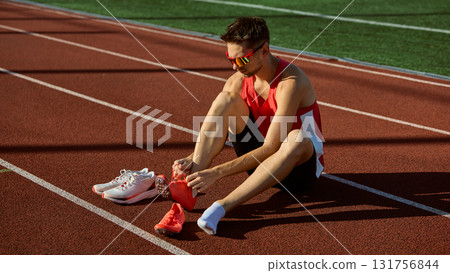 Male athlete putting on red running spikes before training on track field 131756844