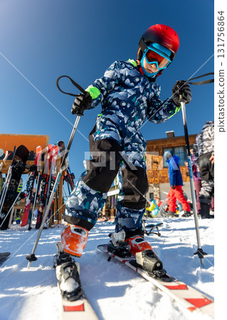 Scenic portrait view kid beginner skier close-up take on ski boots downhill ski slope piste bright warm morning sunrise sky background. Mountain landscape winter resort Scenic portrait view kid beginner skier close-up take on ski boots downhill ski slope piste bright warm morning sunrise sky background. Mountain landscape winter resort 131756864