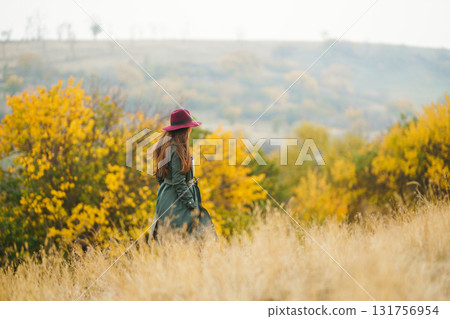 Beautiful stylish girl walks in the autumn park. The girl is dressed in a green coat and a red hat. 131756954