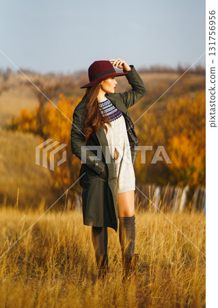 Beautiful stylish girl walks in the autumn park. The girl is dressed in a green coat and a red hat. 131756956