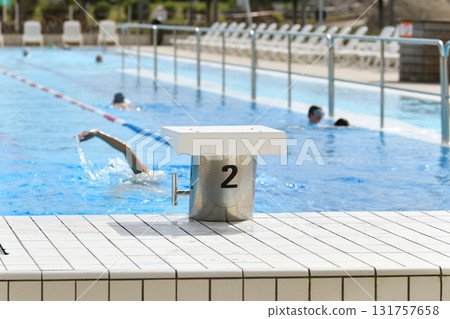 The starting blocks ready to jump into the pool and the swimmers are swimming The starting blocks ready to jump into the pool and the swimmers are swimming 131757658