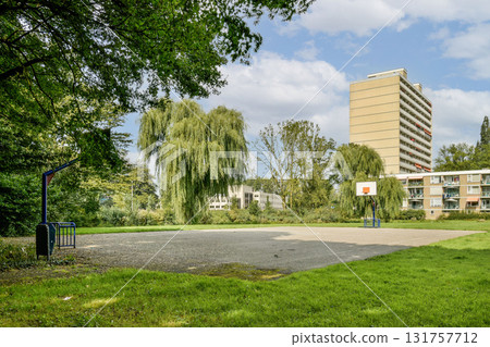 A spacious urban basketball court set amidst lush greenery and modern buildings, providing a vibrant recreational space for sports enthusiasts. 131757712