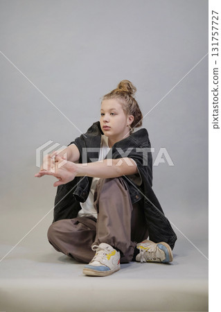 Seated in a relaxed pose, a woman in casual streetwear stretches her arms forward, dressed in a white t-shirt, black denim jacket, and beige pants. This image reflects the modern trend of effortless Seated in a relaxed pose, a woman in casual streetwear stretches her arms forward, dressed in a white t-shirt, black denim jacket, and beige pants. This image reflects the modern trend of effortless 131757727