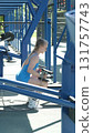 In a blue sports bodysuit, a woman lifts dumbbells at an outdoor gym, focusing on strength training exercises. The photo emphasizes the advantages of combining weight training with outdoor activities 131757743