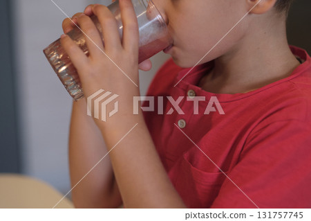 A young boy in a red shirt quenches his thirst with a glass of water, a subtle reminder of the importance of staying hydrated. Perfect for promoting health and hydration. 131757745