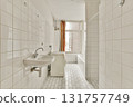 A spacious, minimalist bathroom featuring white tiles, a simple sink, and a freestanding bathtub illuminated by natural light from a window. 131757749