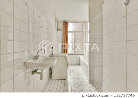 A spacious, minimalist bathroom featuring white tiles, a simple sink, and a freestanding bathtub illuminated by natural light from a window. A spacious, minimalist bathroom featuring white tiles, a simple sink, and a freestanding bathtub illuminated by natural light from a window. 131757749
