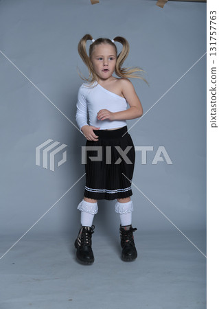 s little girl shows off her bold and joyful personality with a playful pose, making the most of the studio setting. Her trendy one-shoulder top and pleated skirt add a stylish flair to the energetic 131757763