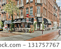 A cozy cafe with outdoor seating nestled within a brick building, surrounded by vibrant greenery and bustling city life. 131757767
