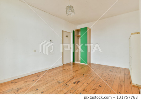 A bright, minimalist room featuring wooden flooring and simple decor. The walls are mostly white with a touch of green in the wardrobe area, providing a calm and spacious feel. 131757768