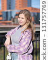 A teenage girl enjoys the sunlight as she poses by a railing, holding headphones in her hand. The photo captures the vibrancy and freedom of youth in an urban setting. 131757769
