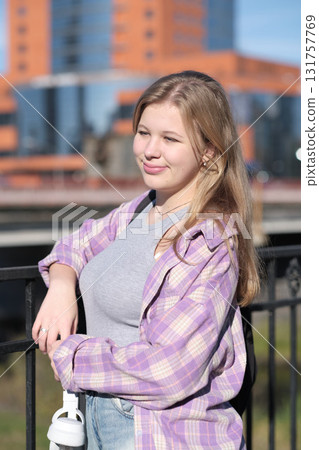 A teenage girl enjoys the sunlight as she poses by a railing, holding headphones in her hand. The photo captures the vibrancy and freedom of youth in an urban setting. A teenage girl enjoys the sunlight as she poses by a railing, holding headphones in her hand. The photo captures the vibrancy and freedom of youth in an urban setting. 131757769