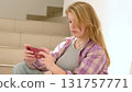 A young woman sitting on stairs smiles while looking at her phone. The image reflects casual moments of digital connection and the joy of staying in touch with loved ones. 131757771