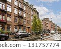 A picturesque street in Amsterdam showcasing typical Dutch architecture, greenery, and a hint of urban life with parked cars and bicycles. 131757774